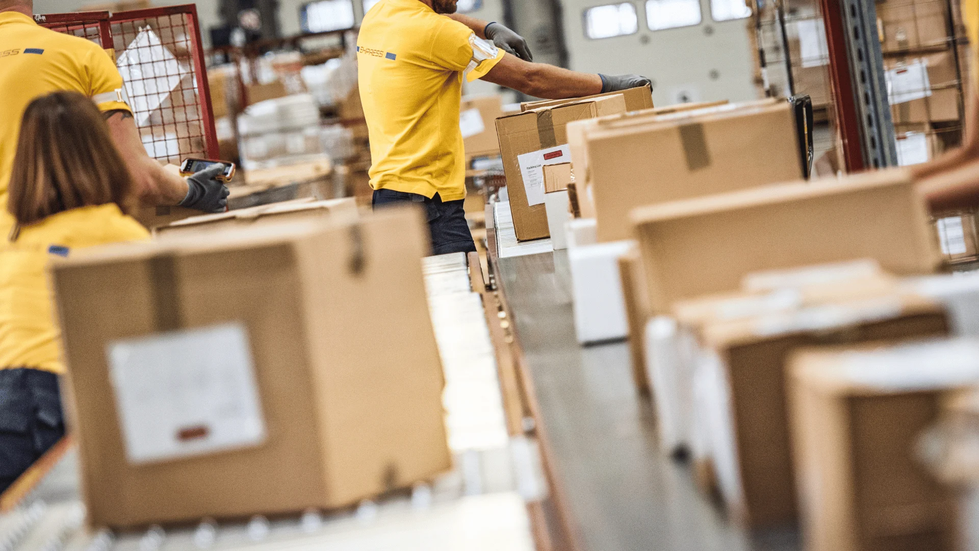 Workers organize and move boxes in a busy warehouse environment.