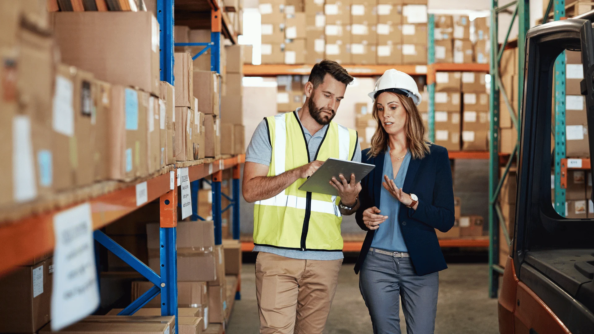 A team of two warehouse workers and a supervisor discuss logistics among packed shelves.